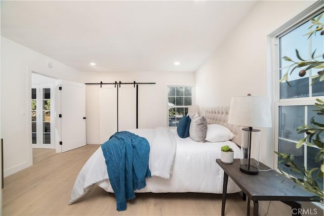 bedroom with a barn door, light wood-type flooring, and multiple windows