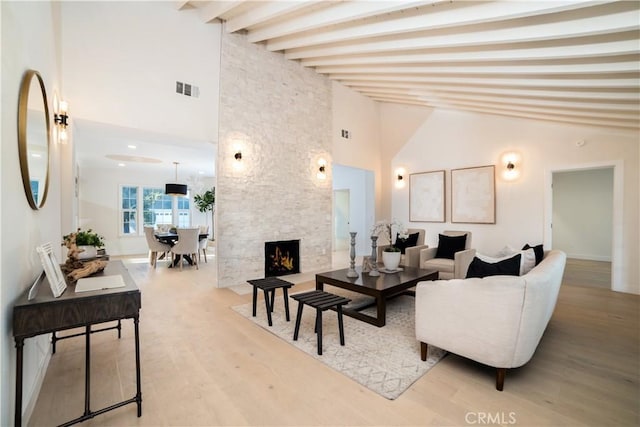 living room featuring high vaulted ceiling, wood-type flooring, beam ceiling, and a stone fireplace