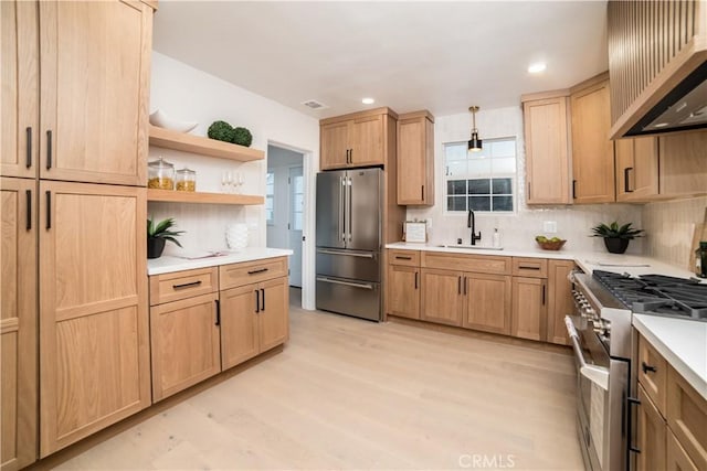 kitchen with premium appliances, wall chimney exhaust hood, sink, backsplash, and light wood-type flooring