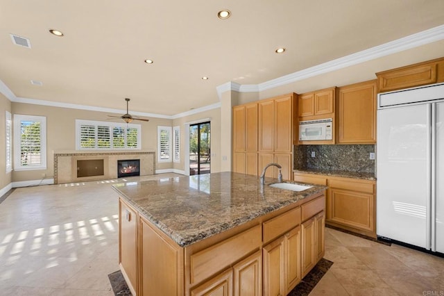 kitchen with light stone countertops, built in appliances, sink, backsplash, and a center island with sink