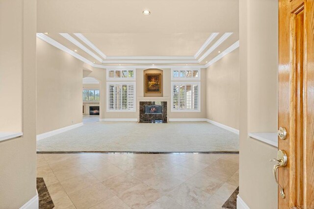 unfurnished living room featuring light carpet, a high end fireplace, ornamental molding, and a tray ceiling