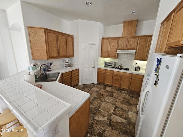 kitchen with sink, tasteful backsplash, tile countertops, white refrigerator, and kitchen peninsula