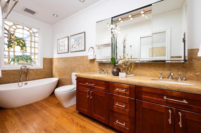 bathroom featuring vanity, wood-type flooring, ornamental molding, a tub to relax in, and toilet