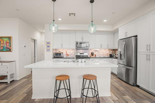 kitchen featuring appliances with stainless steel finishes, backsplash, white cabinetry, and a kitchen island with sink