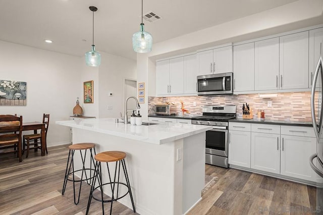 kitchen featuring a center island with sink, white cabinets, stainless steel appliances, and pendant lighting