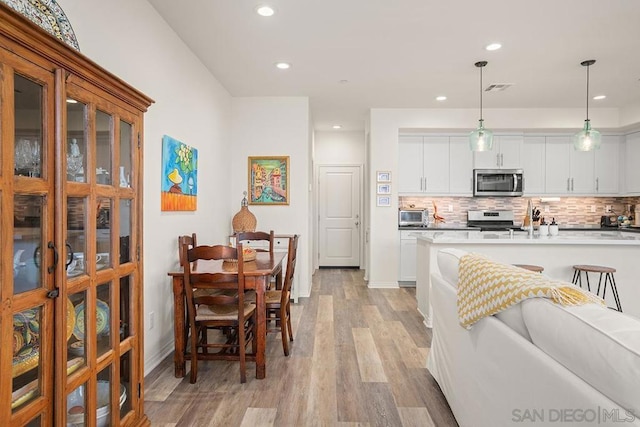 kitchen with decorative light fixtures, white cabinets, gas range oven, and light hardwood / wood-style flooring