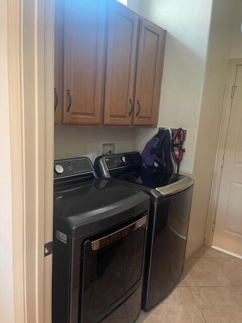 clothes washing area with cabinets, light tile patterned flooring, and washing machine and clothes dryer