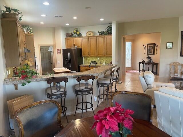 kitchen with kitchen peninsula, tasteful backsplash, a kitchen breakfast bar, black fridge with ice dispenser, and light tile patterned flooring