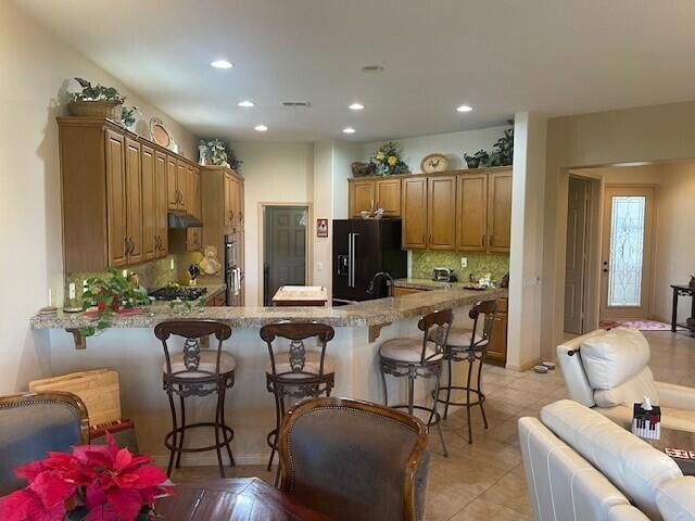 kitchen with light stone countertops, a kitchen bar, tasteful backsplash, black fridge, and kitchen peninsula