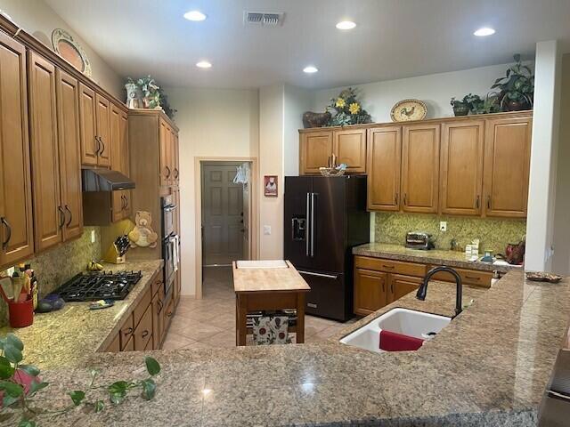 kitchen with decorative backsplash, black fridge with ice dispenser, sink, and stainless steel gas stovetop