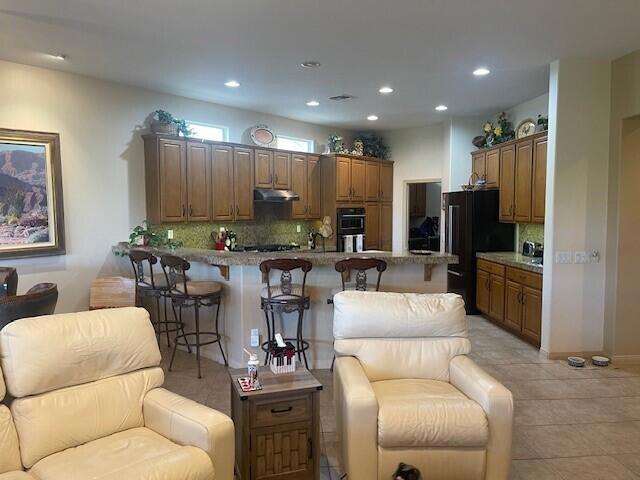 kitchen featuring black refrigerator, backsplash, kitchen peninsula, light tile patterned floors, and a breakfast bar area