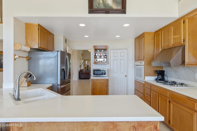 kitchen featuring range hood, kitchen peninsula, decorative backsplash, sink, and appliances with stainless steel finishes