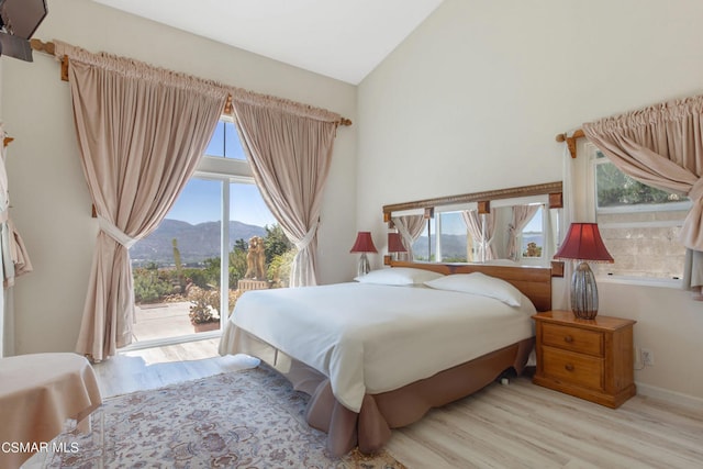 bedroom featuring a mountain view, access to exterior, vaulted ceiling, and light wood-type flooring