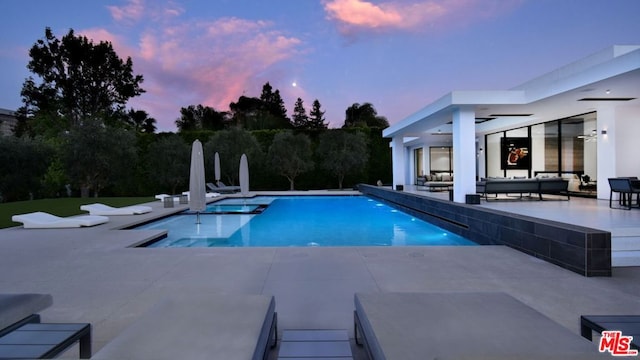 pool at dusk with a patio area, a water slide, and an outdoor living space