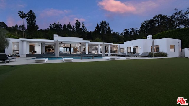 back house at dusk with a patio area and a lawn