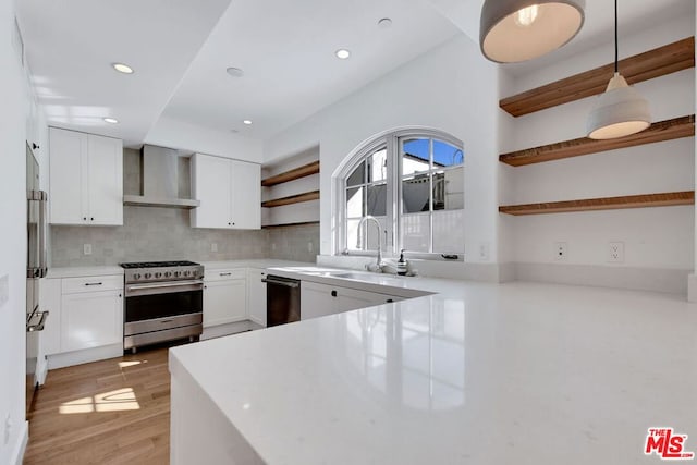 kitchen with appliances with stainless steel finishes, tasteful backsplash, white cabinets, hanging light fixtures, and wall chimney exhaust hood