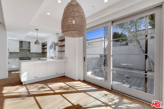 kitchen featuring pendant lighting, white cabinets, decorative backsplash, wall chimney range hood, and light hardwood / wood-style flooring