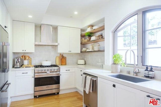 kitchen featuring wall chimney exhaust hood, sink, appliances with stainless steel finishes, decorative backsplash, and white cabinets