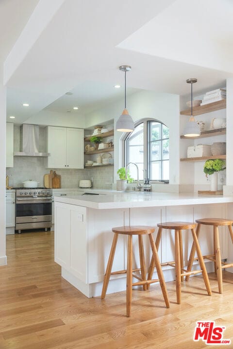 kitchen with wall chimney range hood, high end stainless steel range, a breakfast bar area, and white cabinets