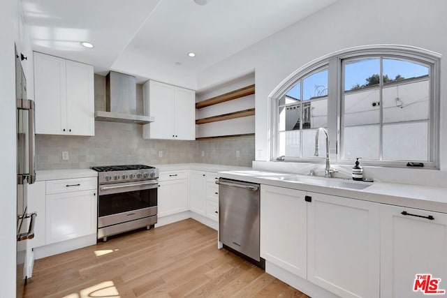 kitchen featuring stainless steel appliances, white cabinetry, wall chimney range hood, and light hardwood / wood-style flooring