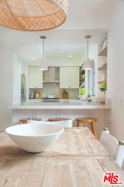 kitchen featuring wall chimney exhaust hood, a breakfast bar, sink, and hanging light fixtures