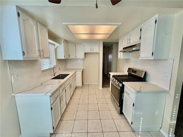 kitchen featuring light tile patterned floors, stainless steel gas range, white cabinets, light stone counters, and sink