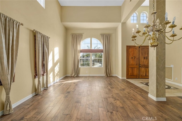 foyer entrance featuring wood-type flooring, plenty of natural light, an inviting chandelier, and a towering ceiling