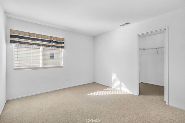 unfurnished bedroom with a closet, a walk in closet, and light colored carpet