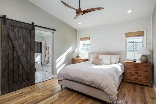 bedroom featuring ceiling fan, wood-type flooring, lofted ceiling, and a barn door