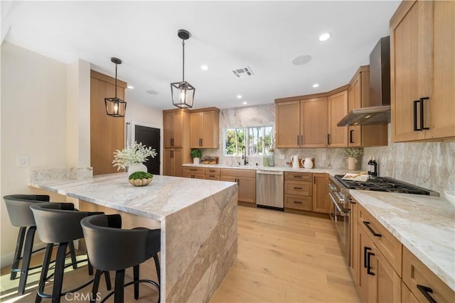 kitchen with a kitchen bar, hanging light fixtures, light stone countertops, stainless steel appliances, and wall chimney exhaust hood