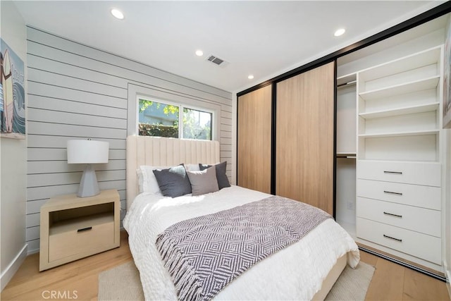 bedroom with light wood-type flooring, a closet, and wood walls