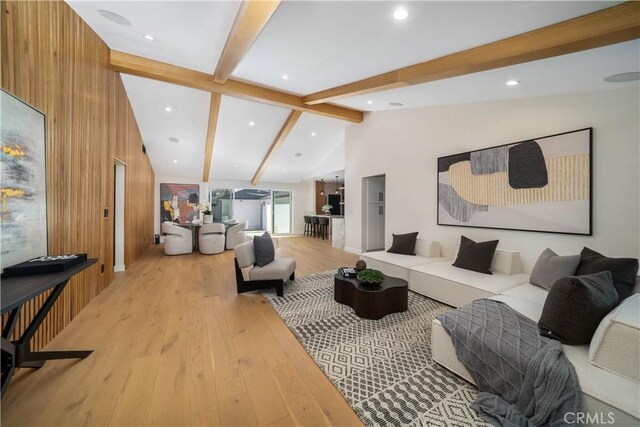 living room featuring light hardwood / wood-style flooring, wooden walls, and vaulted ceiling with beams