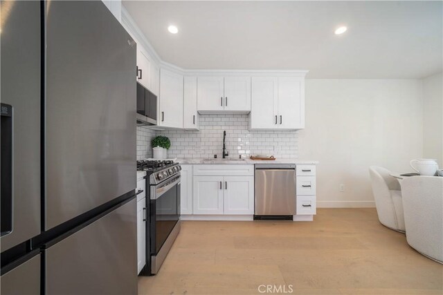 kitchen featuring stainless steel appliances, tasteful backsplash, light wood-type flooring, white cabinets, and sink