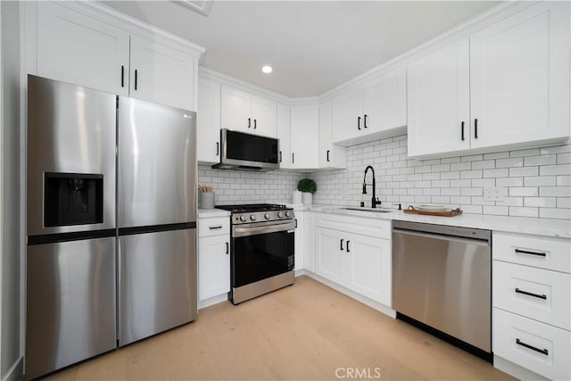 kitchen with white cabinetry, stainless steel appliances, sink, backsplash, and light wood-type flooring