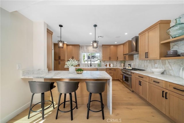 kitchen featuring wall chimney exhaust hood, kitchen peninsula, high end stove, light hardwood / wood-style flooring, and a breakfast bar area