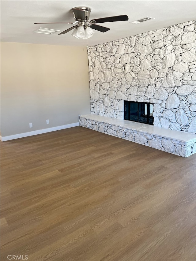 unfurnished living room with hardwood / wood-style flooring, ceiling fan, and a stone fireplace