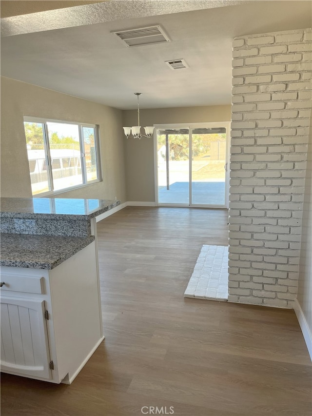 kitchen with decorative light fixtures, white cabinetry, a notable chandelier, light hardwood / wood-style floors, and light stone counters