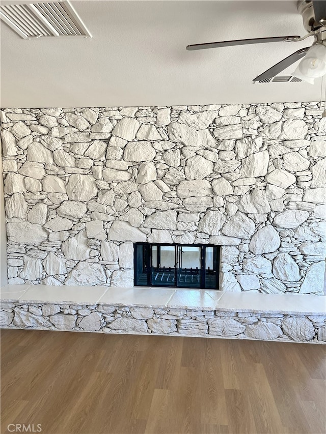 details with hardwood / wood-style flooring, a stone fireplace, and ceiling fan