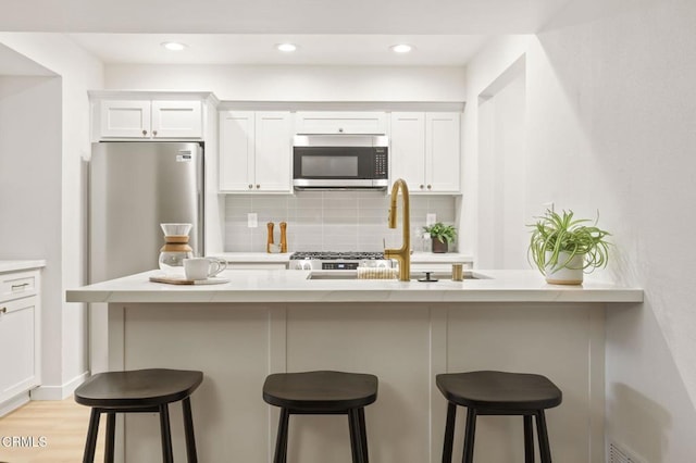 kitchen featuring stainless steel appliances, tasteful backsplash, a kitchen breakfast bar, white cabinets, and sink