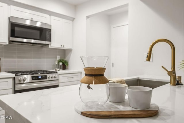 kitchen featuring stainless steel appliances, white cabinets, tasteful backsplash, and light stone countertops