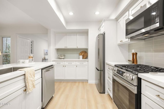 kitchen with white cabinets, decorative backsplash, stainless steel appliances, and light hardwood / wood-style floors