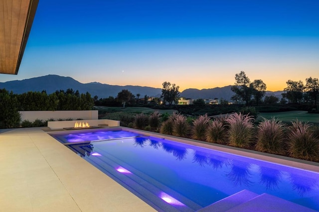 pool at dusk featuring a mountain view and a patio