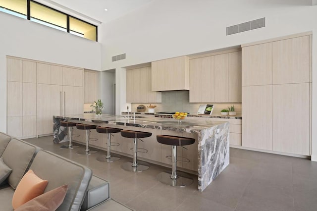 kitchen featuring light stone countertops, a towering ceiling, a kitchen breakfast bar, and a center island with sink