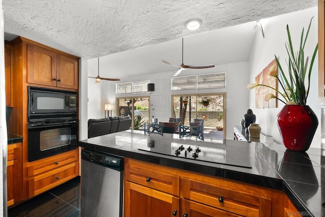 kitchen featuring ceiling fan, dark tile patterned flooring, black appliances, a textured ceiling, and tile counters