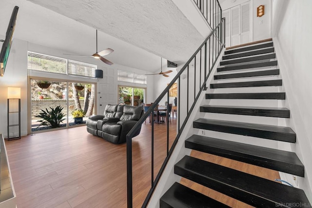 stairway featuring a textured ceiling, ceiling fan, a towering ceiling, and hardwood / wood-style flooring