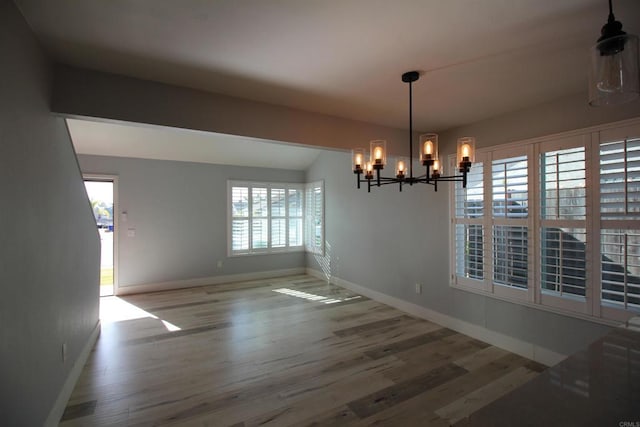 unfurnished dining area with wood-type flooring, a notable chandelier, and vaulted ceiling