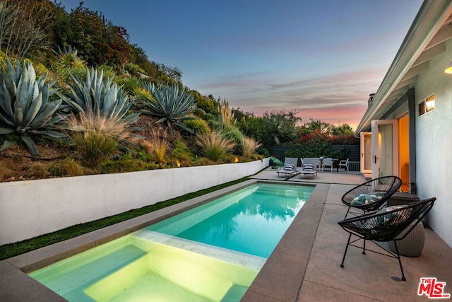 pool at dusk featuring a patio area and an in ground hot tub