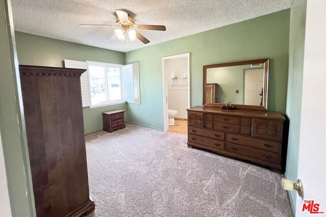 bedroom featuring ceiling fan, light colored carpet, a textured ceiling, and ensuite bath