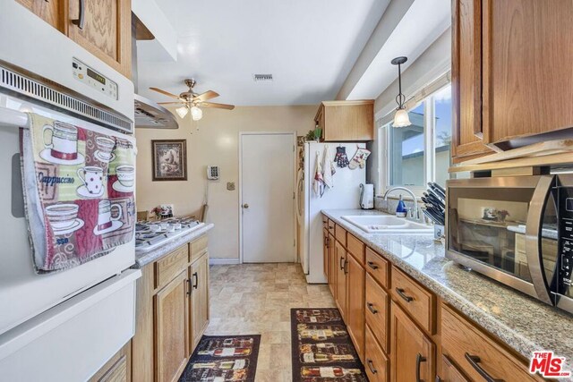 kitchen with ceiling fan, appliances with stainless steel finishes, hanging light fixtures, light stone counters, and sink