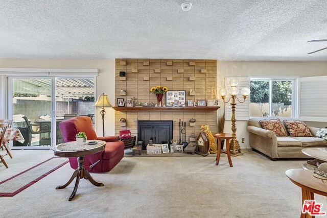 living room with ceiling fan, a textured ceiling, carpet flooring, and a fireplace